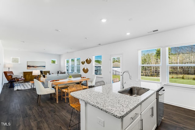 kitchen featuring stainless steel dishwasher, a sink, a center island with sink, visible vents, and dark wood-type flooring