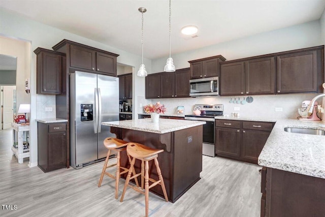 kitchen featuring pendant lighting, backsplash, sink, light wood-type flooring, and appliances with stainless steel finishes