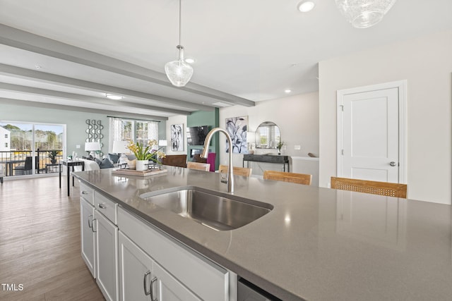 kitchen with beam ceiling, sink, hanging light fixtures, light hardwood / wood-style flooring, and white cabinets