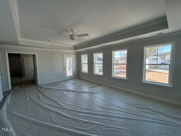 empty room with ceiling fan, a healthy amount of sunlight, and a raised ceiling