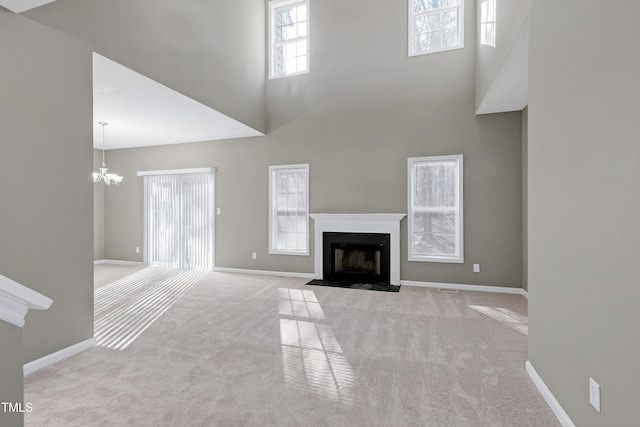 unfurnished living room with an inviting chandelier, light colored carpet, and a towering ceiling