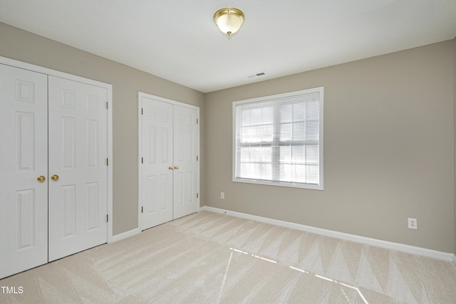 unfurnished bedroom featuring light colored carpet and two closets