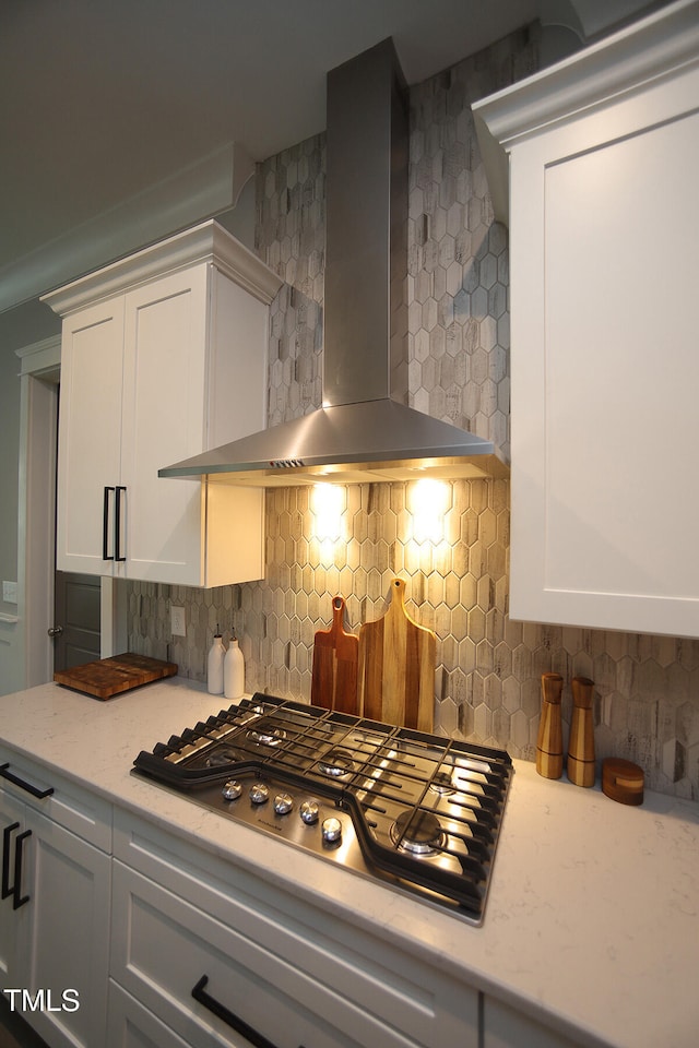 kitchen with stainless steel gas stovetop, wall chimney range hood, decorative backsplash, and white cabinets