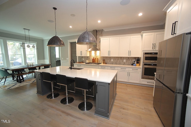 kitchen with white cabinetry, light hardwood / wood-style floors, appliances with stainless steel finishes, and an island with sink