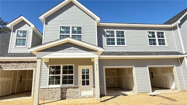 view of front of home featuring an attached garage, stone siding, dirt driveway, and roof with shingles