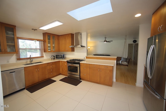 kitchen with ceiling fan, appliances with stainless steel finishes, sink, wall chimney exhaust hood, and decorative light fixtures