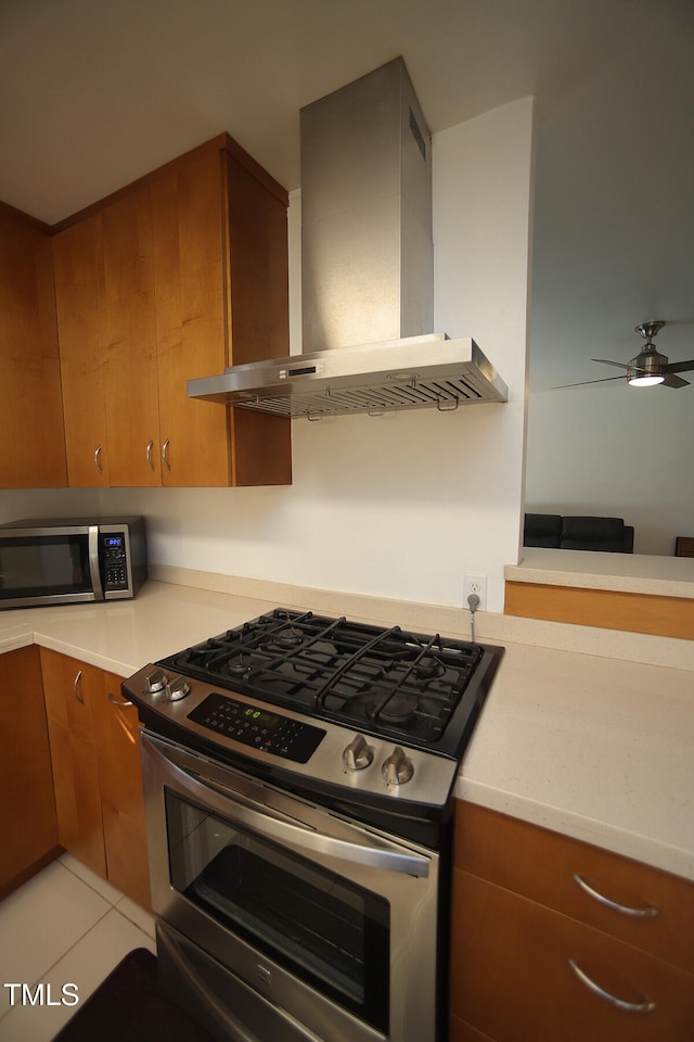 kitchen featuring wall chimney exhaust hood, ceiling fan, stainless steel appliances, and light tile patterned floors