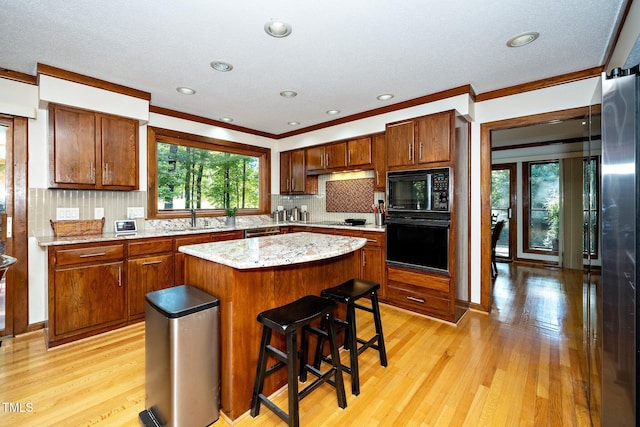 kitchen featuring light hardwood / wood-style floors, black appliances, sink, ornamental molding, and a kitchen island