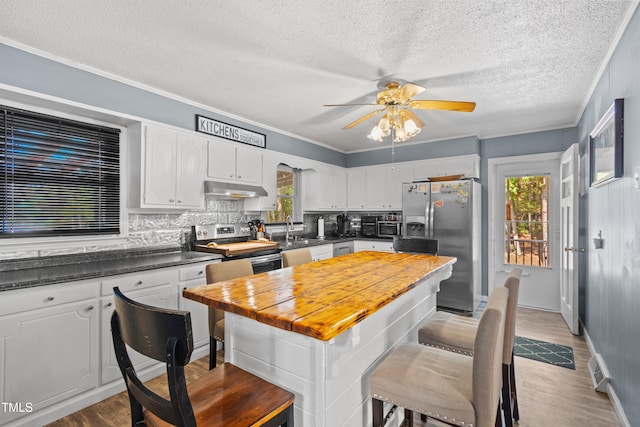 kitchen featuring light wood-type flooring, a textured ceiling, stainless steel appliances, white cabinets, and decorative backsplash