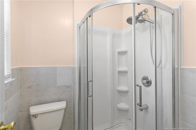 bathroom featuring toilet, tile walls, and a shower with shower door