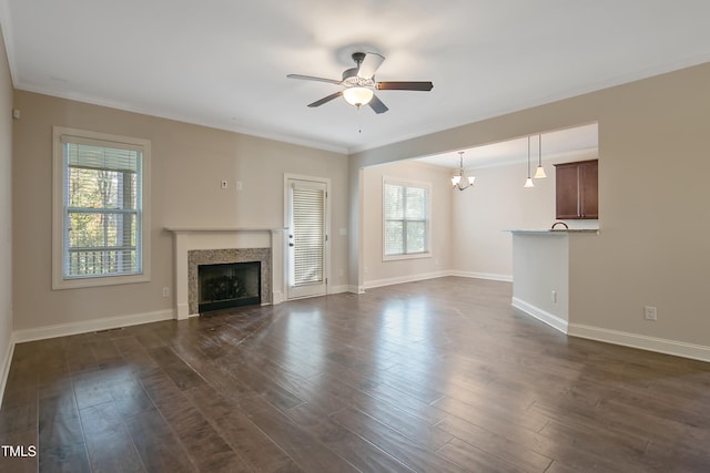 unfurnished living room featuring a wealth of natural light, crown molding, dark hardwood / wood-style floors, and ceiling fan with notable chandelier