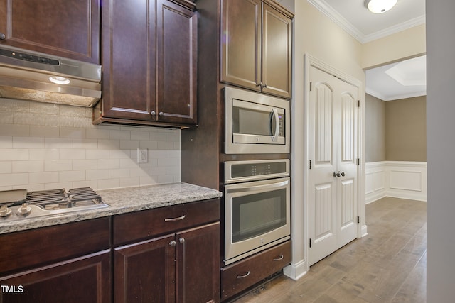 kitchen with tasteful backsplash, stainless steel appliances, range hood, light stone counters, and ornamental molding