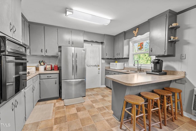 kitchen with gray cabinets, black oven, sink, and stainless steel refrigerator