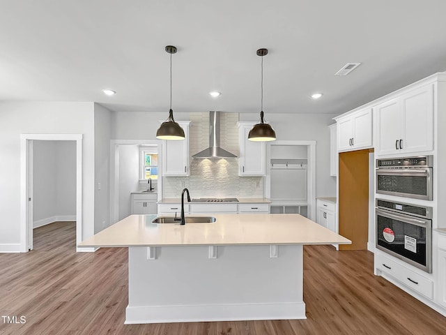 kitchen featuring wall chimney range hood, a sink, white cabinetry, light countertops, and recessed lighting