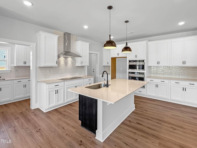 kitchen with a sink, wall chimney exhaust hood, backsplash, wood finished floors, and recessed lighting