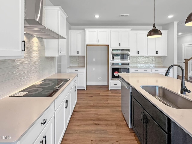 kitchen featuring wall chimney exhaust hood, a sink, stainless steel appliances, white cabinets, and recessed lighting