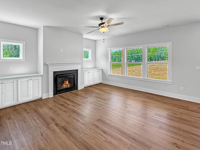 unfurnished living room with ceiling fan, a glass covered fireplace, wood finished floors, and baseboards