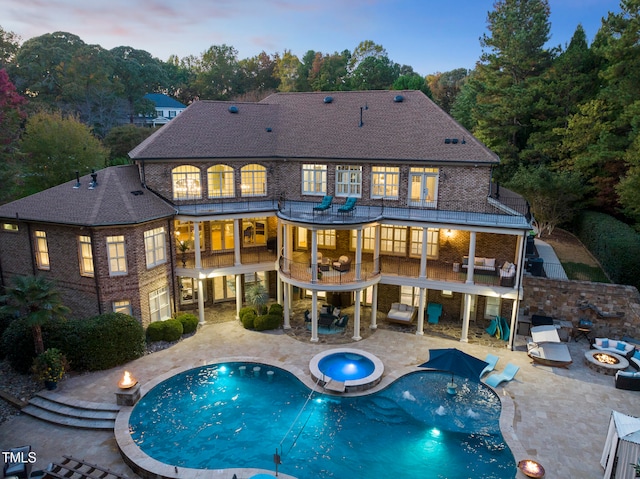 back house at dusk with a swimming pool with hot tub, a balcony, a fire pit, and a patio area