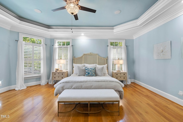 bedroom featuring light wood-type flooring, a raised ceiling, ceiling fan, and crown molding