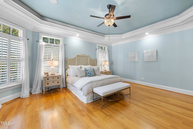 bedroom with ceiling fan, light wood-type flooring, crown molding, and a tray ceiling