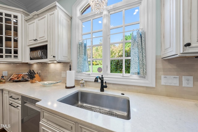 kitchen featuring sink, tasteful backsplash, stainless steel dishwasher, a chandelier, and ornamental molding