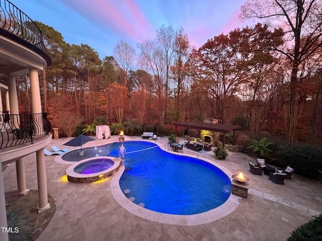 pool at dusk with an in ground hot tub and a patio