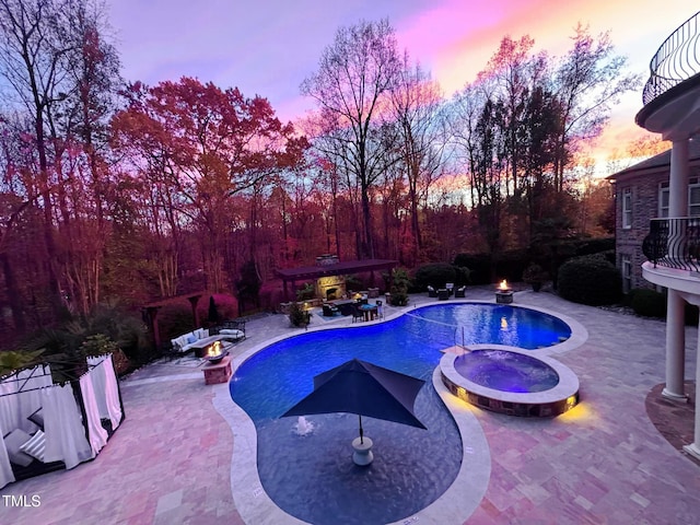 pool at dusk featuring an in ground hot tub and a patio