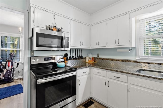 kitchen featuring appliances with stainless steel finishes, crown molding, dark stone counters, white cabinets, and light wood-type flooring