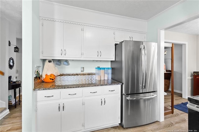 kitchen with light hardwood / wood-style flooring, stainless steel refrigerator, white cabinetry, and dark stone countertops