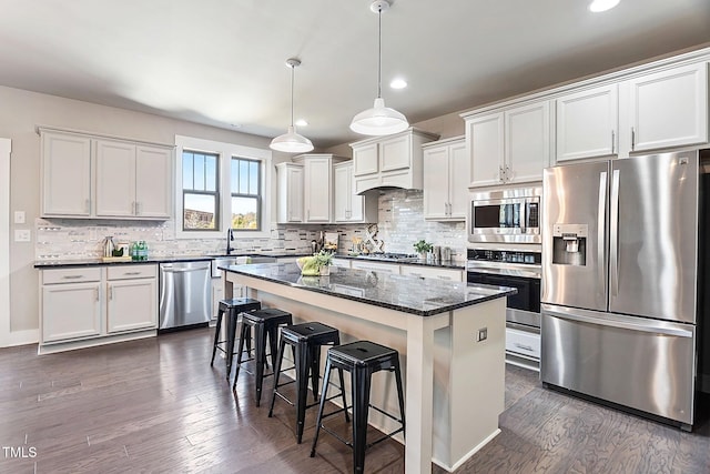 kitchen with a kitchen island, white cabinetry, stainless steel appliances, dark wood-type flooring, and dark stone countertops