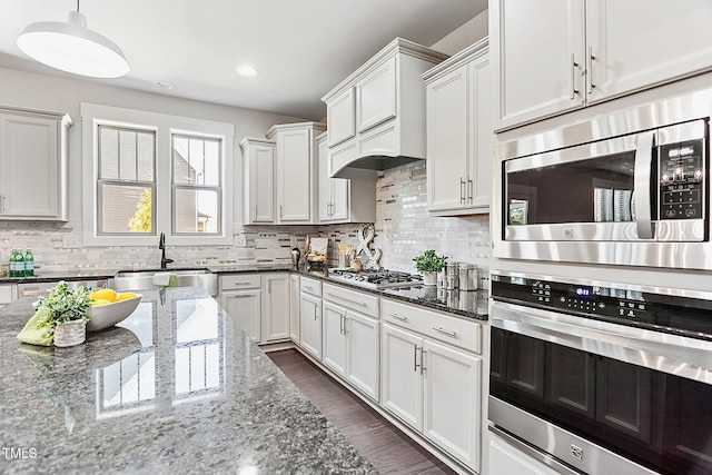 kitchen featuring white cabinets, hanging light fixtures, appliances with stainless steel finishes, dark stone counters, and sink