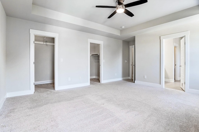 unfurnished bedroom featuring light carpet, a walk in closet, ensuite bathroom, and ceiling fan