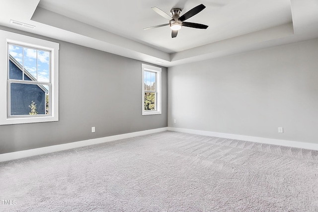 carpeted empty room with ceiling fan, a raised ceiling, and a wealth of natural light