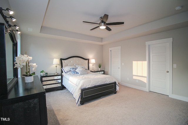 bedroom with light colored carpet, a tray ceiling, and ceiling fan