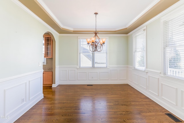 unfurnished dining area with ornamental molding, a chandelier, dark hardwood / wood-style flooring, and a raised ceiling