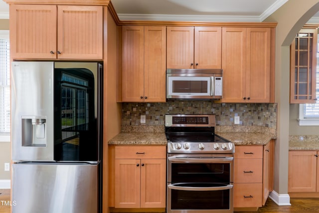 kitchen with crown molding, appliances with stainless steel finishes, light stone countertops, and backsplash