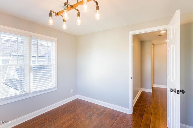 empty room with an inviting chandelier and dark wood-type flooring