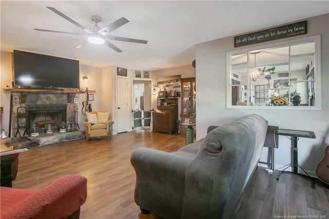 living room with a fireplace, wood finished floors, and ceiling fan with notable chandelier