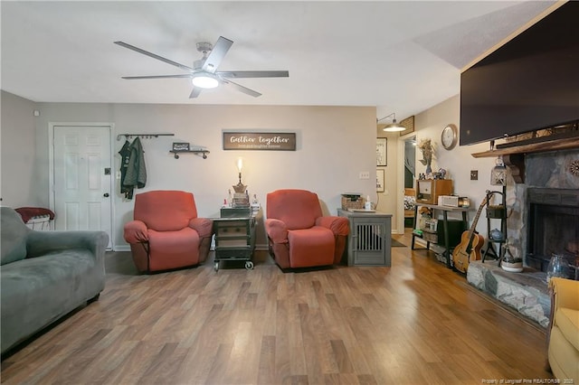 living room featuring ceiling fan, a stone fireplace, and wood finished floors