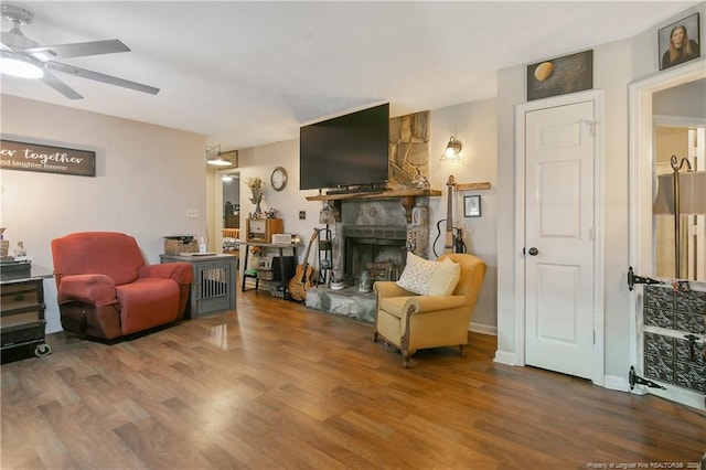 living area with ceiling fan, a fireplace, baseboards, and wood finished floors