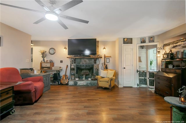 living area featuring a fireplace with raised hearth, ceiling fan, and wood finished floors