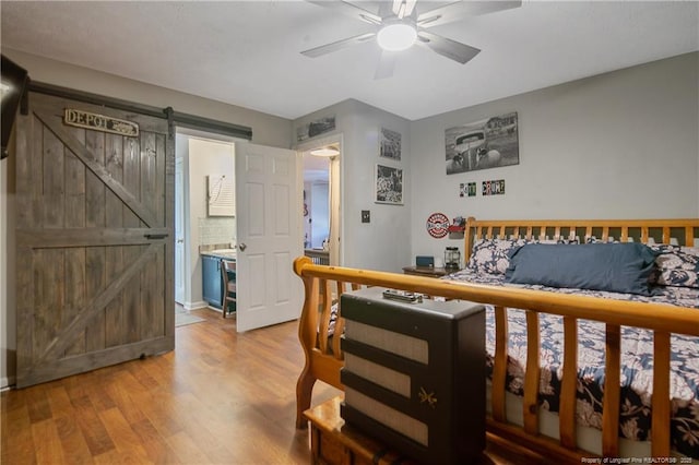 bedroom with a barn door, a ceiling fan, and light wood-style floors