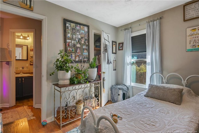 bedroom featuring a sink, baseboards, wood finished floors, and ensuite bathroom