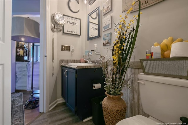 half bathroom featuring baseboards, vanity, toilet, and wood finished floors