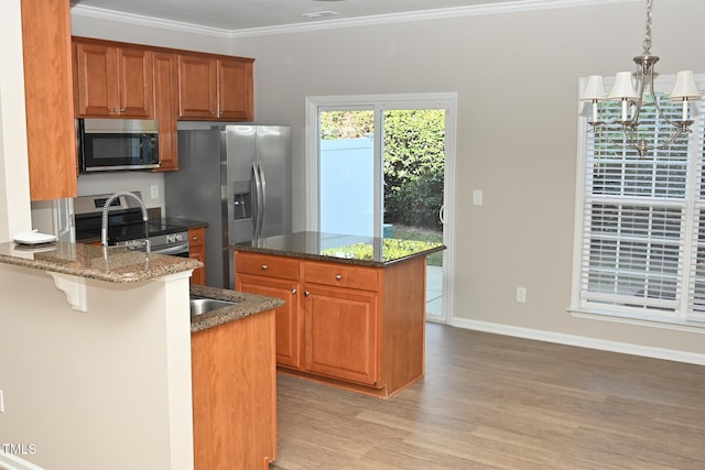 kitchen with hanging light fixtures, dark stone countertops, light wood-type flooring, ornamental molding, and appliances with stainless steel finishes