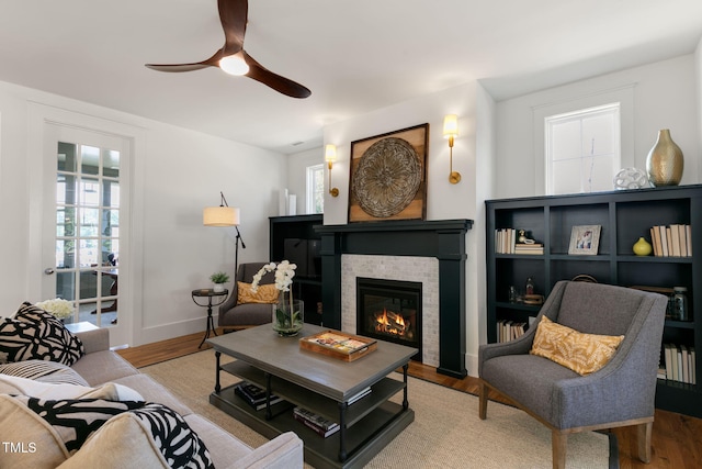 living room featuring ceiling fan, a stone fireplace, and light wood-type flooring