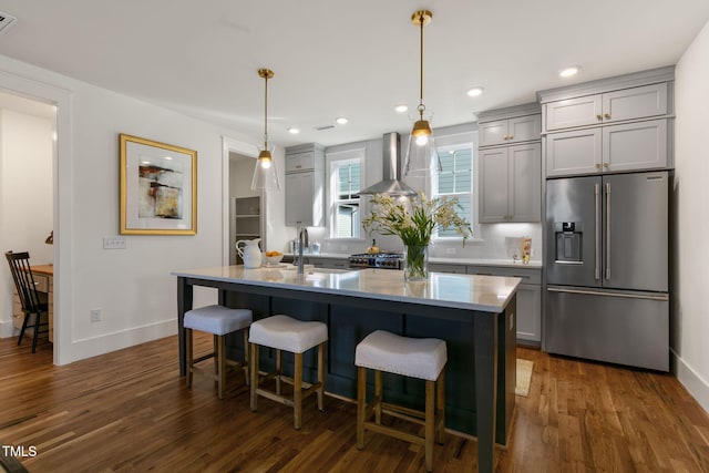 kitchen featuring gray cabinets, wall chimney exhaust hood, stainless steel appliances, and a center island with sink