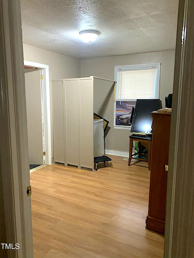 misc room featuring light wood finished floors, a textured ceiling, and baseboards