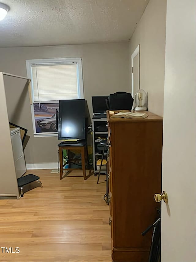 office area with light wood finished floors, a textured ceiling, and baseboards