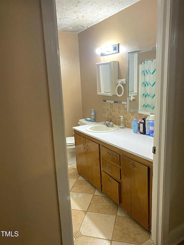 bathroom with tasteful backsplash, vanity, a textured ceiling, tile patterned flooring, and toilet